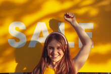 Happy Woman With Hand Raised In Front Of Sale Sign