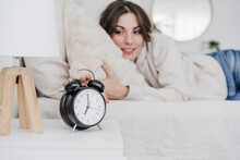 Young Woman Lying On Bed Turning Off Alarm Clock