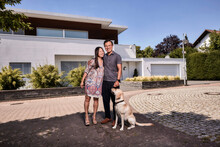 Happy Mature Couple With Dog Standing In Front Of House