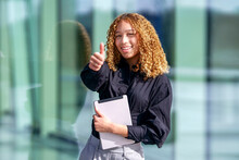 Happy Businesswoman Showing Thumbs Up Gesture Standing In Front Of Glass