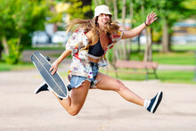 Carefree Woman With Skateboard Jumping At Park