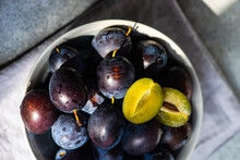 Overhead View Of A Bowl Of Ripe Black Plums On A Folded Napkin