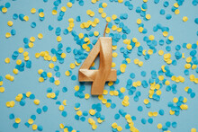 Number 4 Four Golden Celebration Birthday Candle On Yellow And Blue Confetti Background. Four Years Birthday. Concept Of Celebrating Birthday, Anniversary, Important Date, Holiday