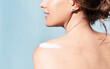 Close up of young female with sunscreen cream on naked shoulder, rear view. Woman with bare shoulders enjoying body care routine on blue background. Skincare treatment and spa cosmetics advertising.