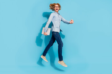 Full length photo of busy hurrying man wear denim shirt spectacles jumping holding modern device isolated blue color background
