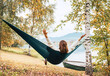 © Soloviova Liudmyla - The young woman cheerfully rose arms up while she swinging in a hammock between the birch trees on the mountain lake bank. Out-of-town Outdoor Recreation in Nature concept image.