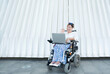 © Renata Hamuda - smiling woman in wheelchair uses laptop outdoors for a video conference on a white background, remote work providing job opportunities for disabled people