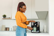 © Prostock-studio - Excited young black woman making fresh aromatic coffee in modern machine in kitchen interior