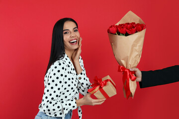 Poster - Happy woman receiving tulip bouquet from man on red background. 8th of March celebration