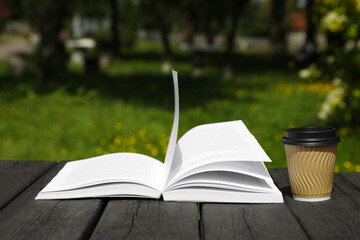 Open book and paper coffee cup on wooden table outdoors
