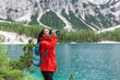 © Andrei - Hydration while on track. Attractive woman hiker in red raincoat drinking water near a lake and mountains