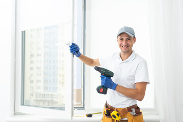 Wall Mural - Master in gloves adjusting pvc windows with screwdriver closeup. Installation of plastic windows repair and maintenance concept.