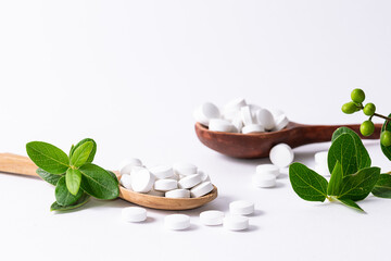 Wall Mural - Natural herbal medicine concept. Two wooden spoons with natural medical capsules for healthy lifestyle and immunity support and fresh green leaves on white background close up.