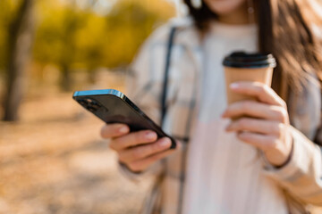 close-up hands holding phone of young woman walking in autumn park using app on smartphone