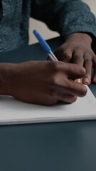 Poster - Vertical video: Close up of african american black person taking notes on notepad using a pen. Male adult hands of remote worker writing text on white paper