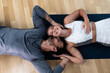 © Srdjan - Young happy married couple man and woman lying on the floor on yoga mats after home workout training. Positive active people in their apartment sweaty after exercising.