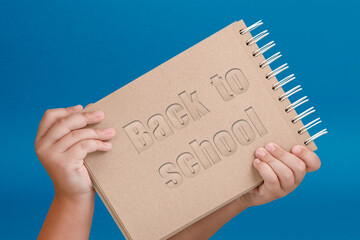 Wall Mural - Notepad in hand with text back to school. Notepad in the hands of a child on a blue background. Hands hold a book as a symbol of the beginning of the school year and the day of knowledge.