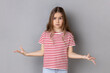 What do you want? Portrait of little girl wearing striped T-shirt standing with raised hands and surprised indignant expression, asking what reason. Indoor studio shot isolated on gray background.