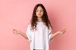 Portrait of relaxed little girl wearing white T-shirt doing yoga, breathing, keeping eyes closed, calming down after hard lessons. Indoor studio shot isolated on pink background.