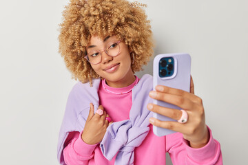 Wall Mural - indoor shot of pretty woman with curly hair makes selfie or has video conference via cellular takes 