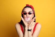 Fashionable Young Woman In Pin Up Outfit Blowing Bubblegum On Yellow Background
