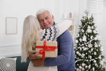 Canvas Print - Happy mature couple with gift box hugging at home. Christmas celebration