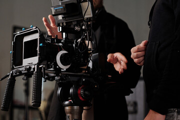 Modern steadicam against videographer and his assistant in black casualwear discussing working moments in studio