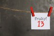 Paper note with phrase Friday! 13 hanging on twine against grey background, space for text. Bad luck superstition