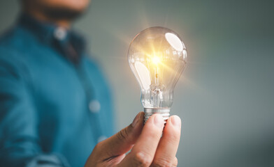 Poster - Idea innovation and inspiration concept. Hand of man holding illuminated light bulb, concept creativity with bulbs that shine glitter. Inspiration of ideas for sustainable business development...