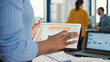 © DC Studio - Closeup of african american woman hands picking up tablet interacting with touchscreen looking at erp software interface standing at desk. Selective focus on startup employee holding digital device.