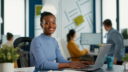 Poster - portrait of african american woman typing using laptop keyboard and smiling at camera sitting at des