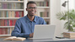 © stockbakers - Young African Man Smiling at Camera while using Laptop