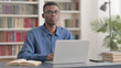 © stockbakers - Young African Man Looking at Camera while using Laptop