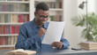 © stockbakers - Young African Man Celebrating Success while Reading Documents in Office