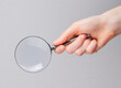 Magnifying glass lens in female hand close up over gray background