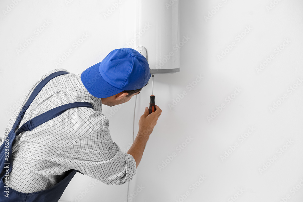 Young plumber repairing boiler with screwdriver in bathroom