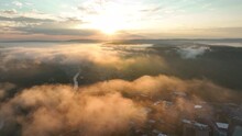 Aerial Flight Above Clouds At Sunrise. River And City Town Buildings Below.