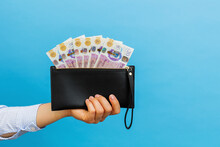 Female Hands Holding British Pounds Banknotes In Black Wallet On A Blue Background.