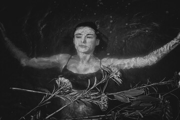 Wall Mural - Black and white photo of a girl in a swimsuit who is in the water and under the water near her floating flowers.