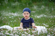 Baby boy in a blue bandana on head sitting on the green grass in the park summer day. Cheerful little kid sitting on blanket.