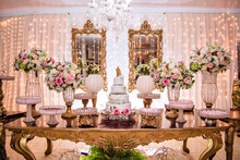 A Table Decorated With Flowers And Sweets And A White Wedding Cake Decorated With Roses And A Golden Biscuit Wedding Couple On Top