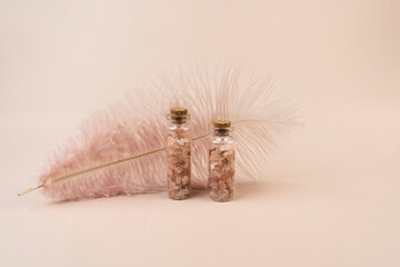 Two glass bottles with pink salt for spa procedures standing on a pink background, a pink feather behind them