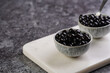 Cooked tapioca pearls for trendy bubble boba ice tea in two small grey ceramic bowls on marble board on dark grey concrete background