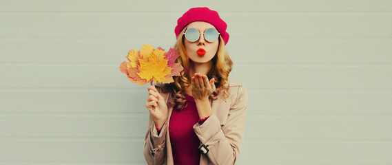 autumn portrait of beautiful young woman model with yellow maple leaves blowing her lips with lipsti