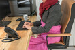 Leinwandbild Motiv Eine Frau schützt sich mit Decke, Wärmfläsche, Schal und heißem Tee am Schreibtisch vor der Kälte bei der Arbeit, Konzept Energiekosten, Energiesparen durch Absenken der Raumtemperatur
