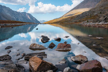 Tranquil Autumn Landscape With Clouds Reflection On Smooth Mirror Surface Of Mountain Lake In High Hanging Valley. Meditative View From Calm Alpine Lake To Mountain Vastness. Stones In Clear Water.