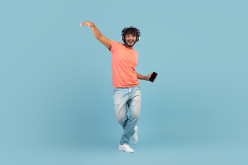 Wall Mural - Happy eastern guy using wireless headset and smartphone, dancing