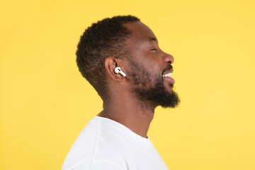 Happy African Man Listening Music Wearing Earbuds Over Yellow Background