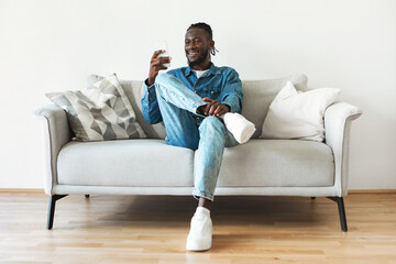 Wall Mural - African American Guy Using Smartphone Sitting On Couch At Home