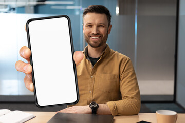 Poster - Handsome Young Businessman Showing Blank Smartphone While Sitting At Desk In Office